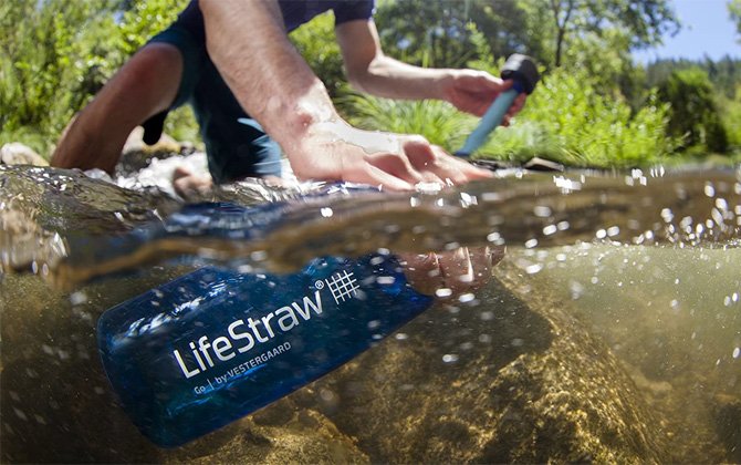 Botella filtrante de agua LifeStraw Go abierta y sumergida en un arroyo.  La otra mano de la persona es la parte superior y muestra la parte superior con la pajilla del filtro.